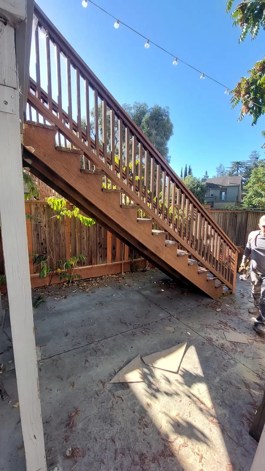 Exterior deck staircase with most treads missing from the stringers, a worker with a drill at the foot of it