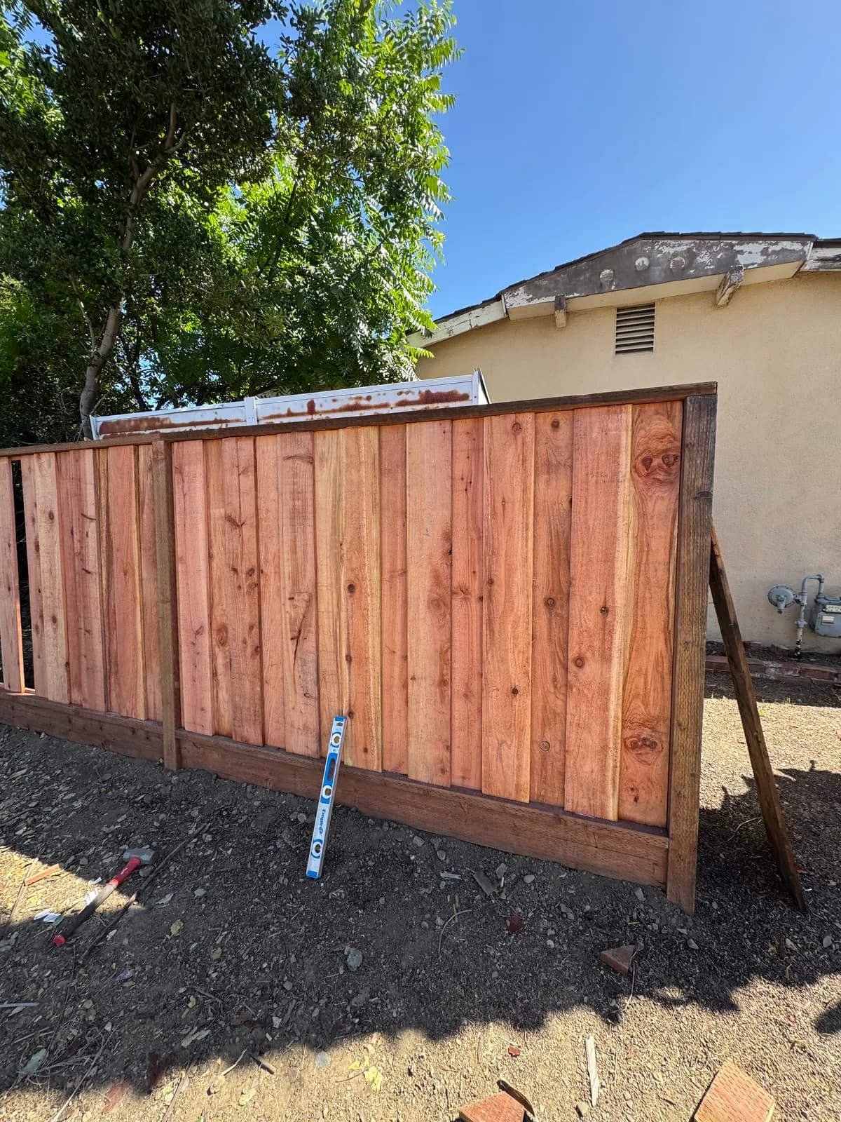 Finished fence bay with its end post held by a diagonal brace against a rendered wall, open frame continuing to the left