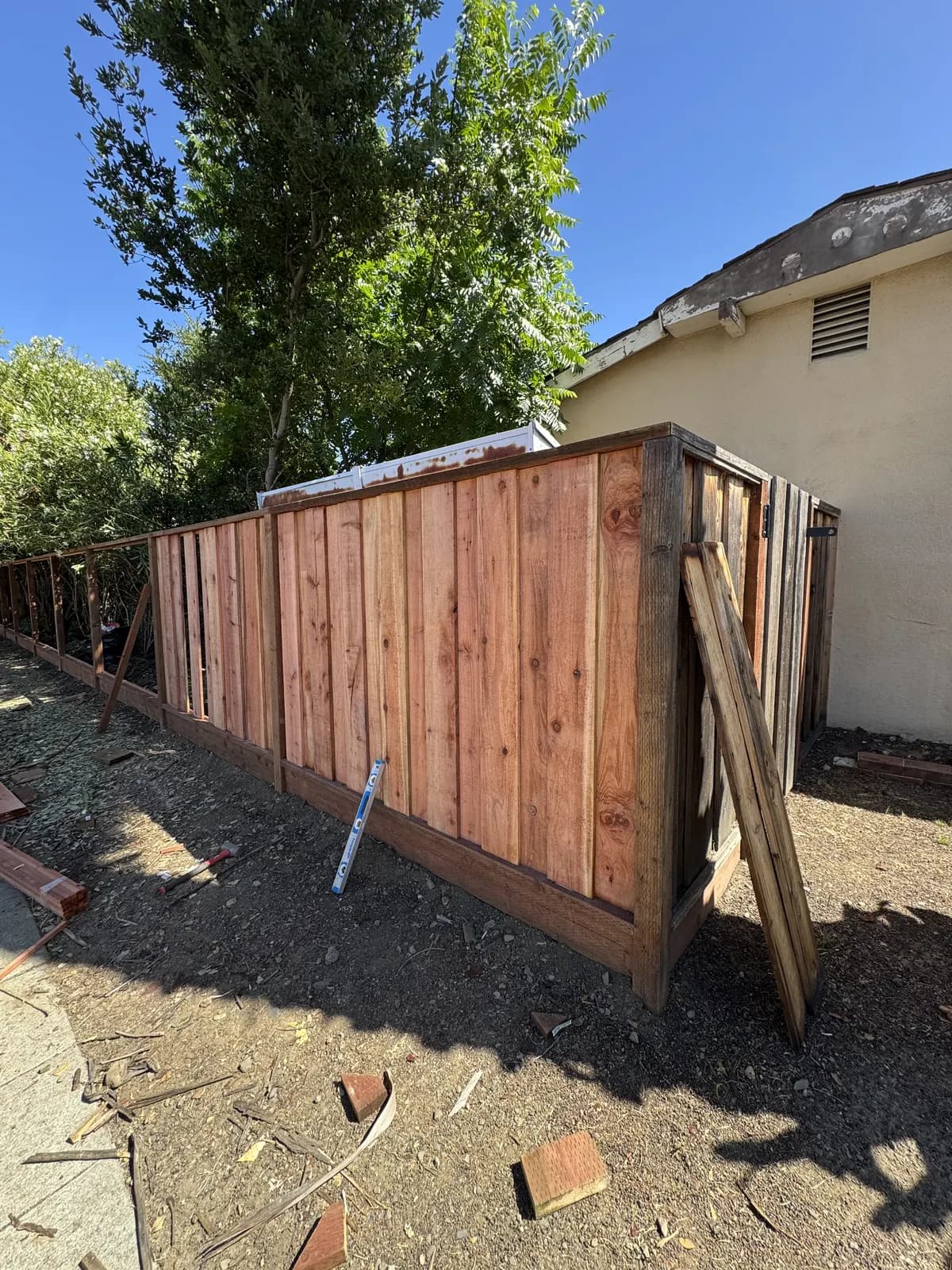 New redwood boards fitted along part of a fence run beside an old grey section, spirit level leaning against the boards