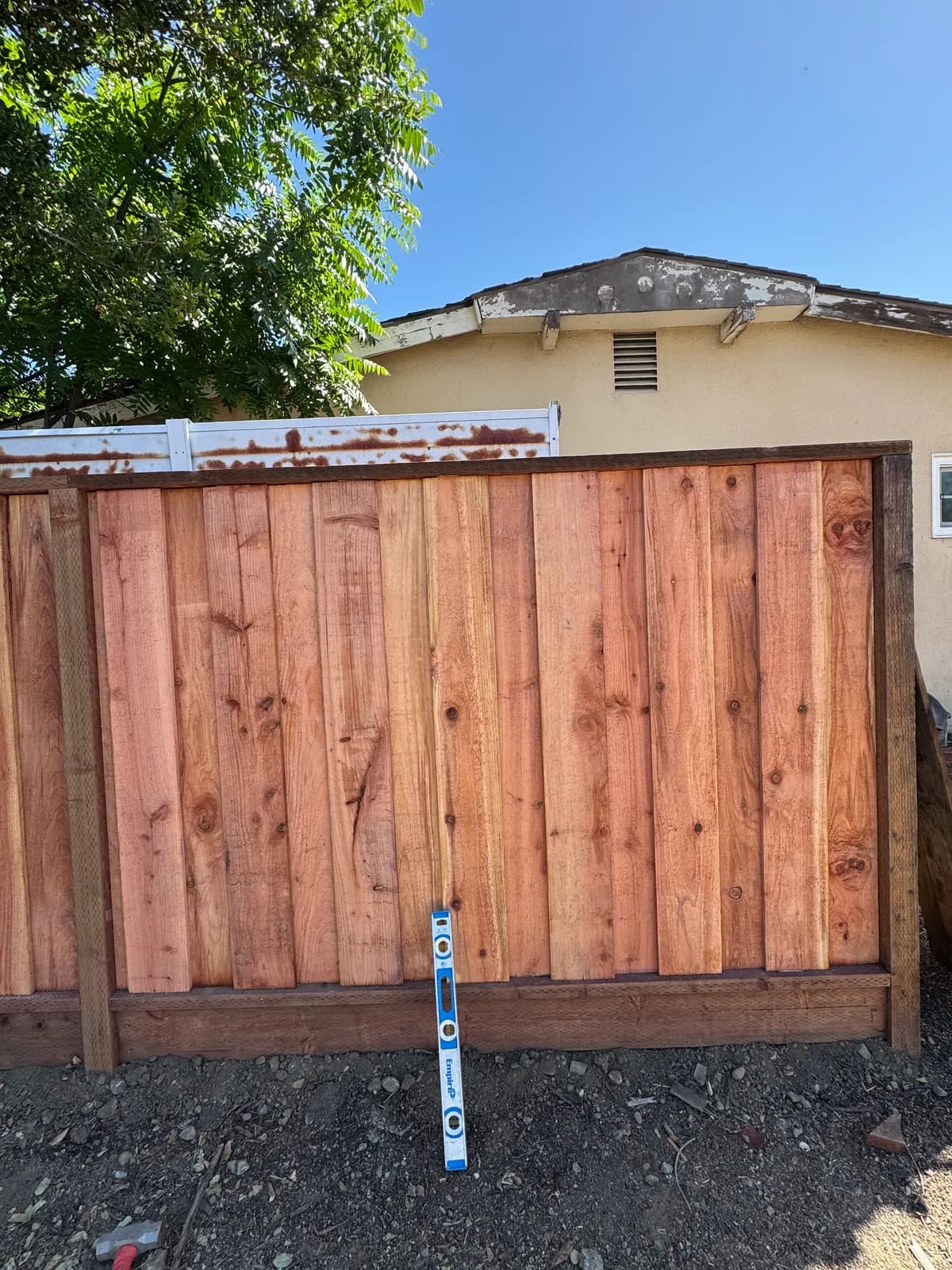 Finished bay of redwood fence with a dark cap rail on top and a kickboard along the bottom, spirit level leaning against it