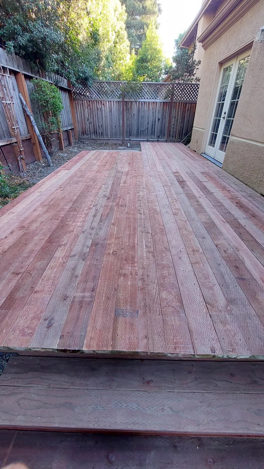 Redwood deck surface running to a house wall with French doors, old grey lattice-topped fence along the far side